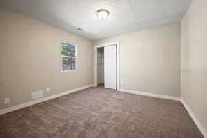 Unfurnished bedroom with a textured ceiling, carpet floors, and a closet