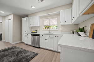 Kitchen featuring white cabinetry, dishwasher, sink, light hardwood / wood-style floors, and a textured ceiling