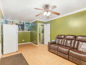 Living room with ceiling fan, light tile patterned floors, and crown molding