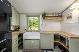 Kitchen featuring green cabinetry, decorative backsplash, sink, and wooden counters