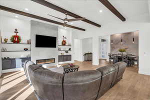 Living room featuring beam ceiling, a tiled fireplace, ceiling fan, and light wood-type flooring