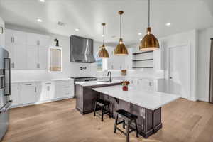 Kitchen with appliances with stainless steel finishes, wall chimney exhaust hood, an island with sink, and light hardwood / wood-style floors