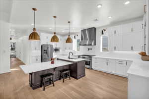 Kitchen with high quality appliances, a center island with sink, sink, wall chimney exhaust hood, and light wood-type flooring