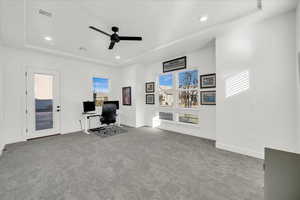 Carpeted office space with a tray ceiling and ceiling fan