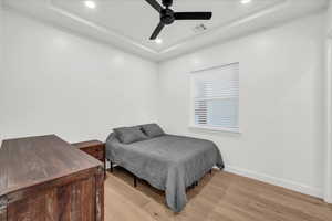 Bedroom featuring light hardwood / wood-style floors, a raised ceiling, and ceiling fan