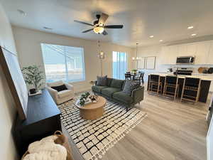 Living room featuring ceiling fan with notable chandelier and light hardwood / wood-style floors