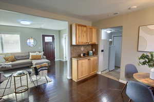 Kitchen featuring dark hardwood / wood-style floors, white refrigerator with ice dispenser, light brown cabinetry, and tasteful backsplash