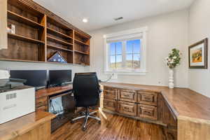 Home office with built in desk and dark wood-type flooring