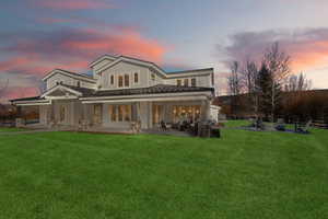 Back house at dusk with french doors, a yard, a patio area, and exterior kitchen