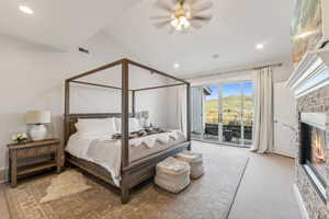 Carpeted bedroom with ceiling fan, access to exterior, and a brick fireplace