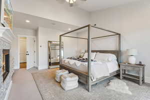 Carpeted bedroom with a stone fireplace and ceiling fan