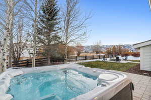 Snow covered pool featuring a mountain view, a patio, and a hot tub