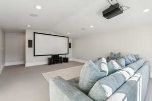 Carpeted home theater room with vaulted ceiling