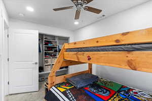 Carpeted bedroom with ceiling fan and a closet