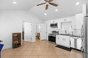 Kitchen featuring stainless steel appliances, ceiling fan, sink, white cabinetry, and lofted ceiling