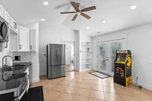 Kitchen with white cabinetry, sink, vaulted ceiling, light tile patterned floors, and appliances with stainless steel finishes