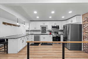 Kitchen with a kitchen bar, white cabinets, stainless steel appliances, and light hardwood / wood-style floors