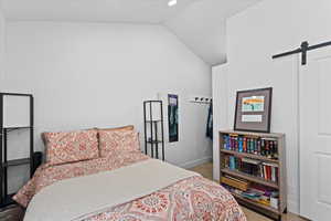 Tiled bedroom featuring a barn door and vaulted ceiling