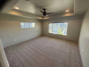 Carpeted empty room featuring a textured ceiling, a raised ceiling, and ceiling fan