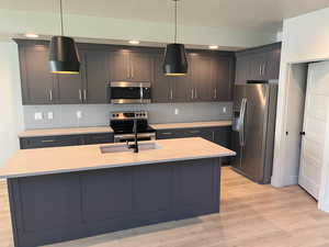 Kitchen featuring appliances with stainless steel finishes, a center island with sink, light hardwood / wood-style flooring, and hanging light fixtures