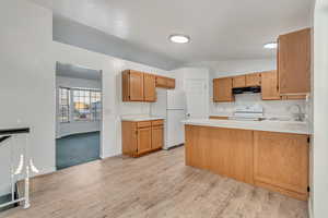 Kitchen featuring lofted ceiling, white appliances, sink, light wood-type flooring, and kitchen peninsula