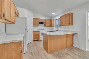 Kitchen featuring white appliances, sink, vaulted ceiling, light wood-type flooring, and kitchen peninsula