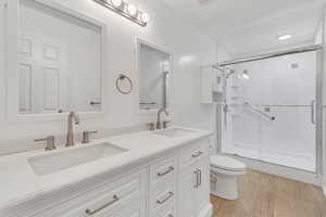 Bathroom with hardwood / wood-style floors, vanity, a shower with shower door, and toilet