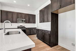 Kitchen with sink, light stone counters, backsplash, appliances with stainless steel finishes, and light wood-type flooring