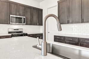 Kitchen featuring sink, stainless steel appliances, light stone counters, backsplash, and dark brown cabinets