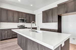 Kitchen with light stone countertops, appliances with stainless steel finishes, light hardwood / wood-style flooring, and sink