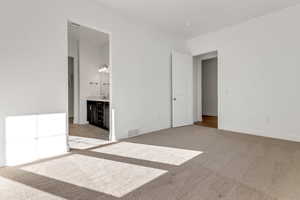 Unfurnished bedroom featuring ensuite bathroom, sink, and light colored carpet