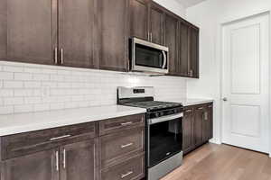 Kitchen featuring appliances with stainless steel finishes, light wood-type flooring, light stone counters, and dark brown cabinetry