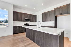 Kitchen featuring a center island with sink, sink, stainless steel appliances, and light hardwood / wood-style flooring