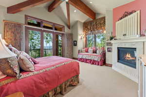 Carpeted bedroom with a tiled fireplace, lofted ceiling with beams, and access to exterior