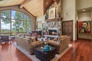 Living room with beamed ceiling, a stone fireplace, wood-type flooring, and high vaulted ceiling