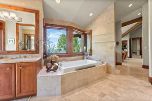 Bathroom featuring vanity, tile walls, tiled tub, and vaulted ceiling