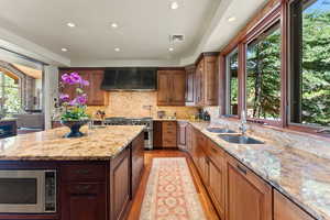 Kitchen with a kitchen island with sink, wall chimney exhaust hood, light wood-type flooring, appliances with stainless steel finishes, and light stone counters