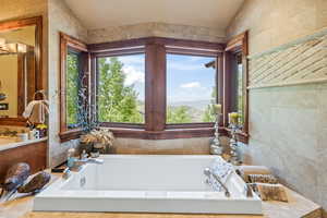 Bathroom featuring a mountain view, tiled bath, tile walls, and lofted ceiling