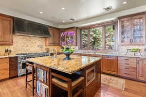 Kitchen featuring light stone counters, wall chimney range hood, a breakfast bar area, and appliances with stainless steel finishes