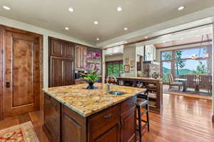 Kitchen featuring light stone countertops, sink, hardwood / wood-style floors, oven, and a center island with sink