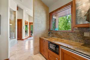 Bar with black microwave, sink, tasteful backsplash, light stone counters, and light tile patterned floors