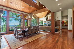 Dining space with wood-type flooring, beam ceiling, an inviting chandelier, high vaulted ceiling, and a stone fireplace