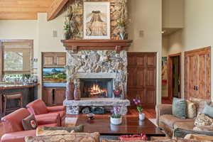 Living room featuring wooden ceiling, a high ceiling, a stone fireplace, beamed ceiling, and hardwood / wood-style floors