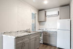 Kitchen with white appliances, dark wood-type flooring, sink, gray cabinets, and a wall unit AC