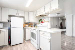 Kitchen with white appliances, light hardwood / wood-style flooring, and white cabinetry