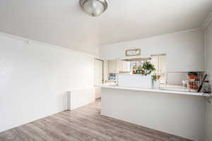 Kitchen with kitchen peninsula, crown molding, and light wood-type flooring