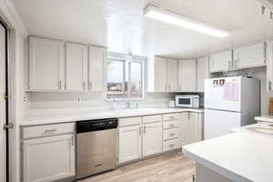 Kitchen featuring white appliances, sink, light wood-type flooring, a textured ceiling, and white cabinetry