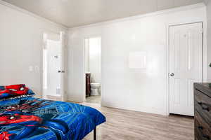 Bedroom with ensuite bath, ornamental molding, and light hardwood / wood-style flooring