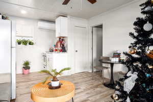 Kitchen with light hardwood / wood-style flooring, a wall mounted AC, white fridge, white cabinets, and ornamental molding