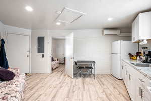 Kitchen featuring electric panel, light hardwood / wood-style flooring, white cabinets, and a wall mounted AC